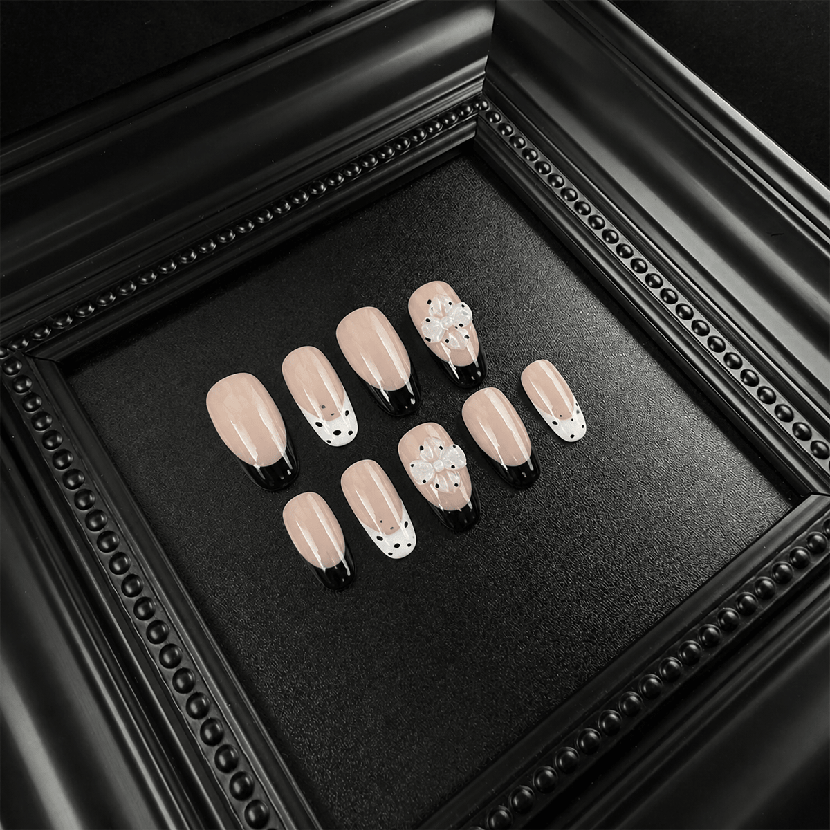 Nude press-on nails with glossy black French tips and white splatter
