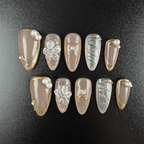 Nude almond press-on nails with gold trim and 3D flowers